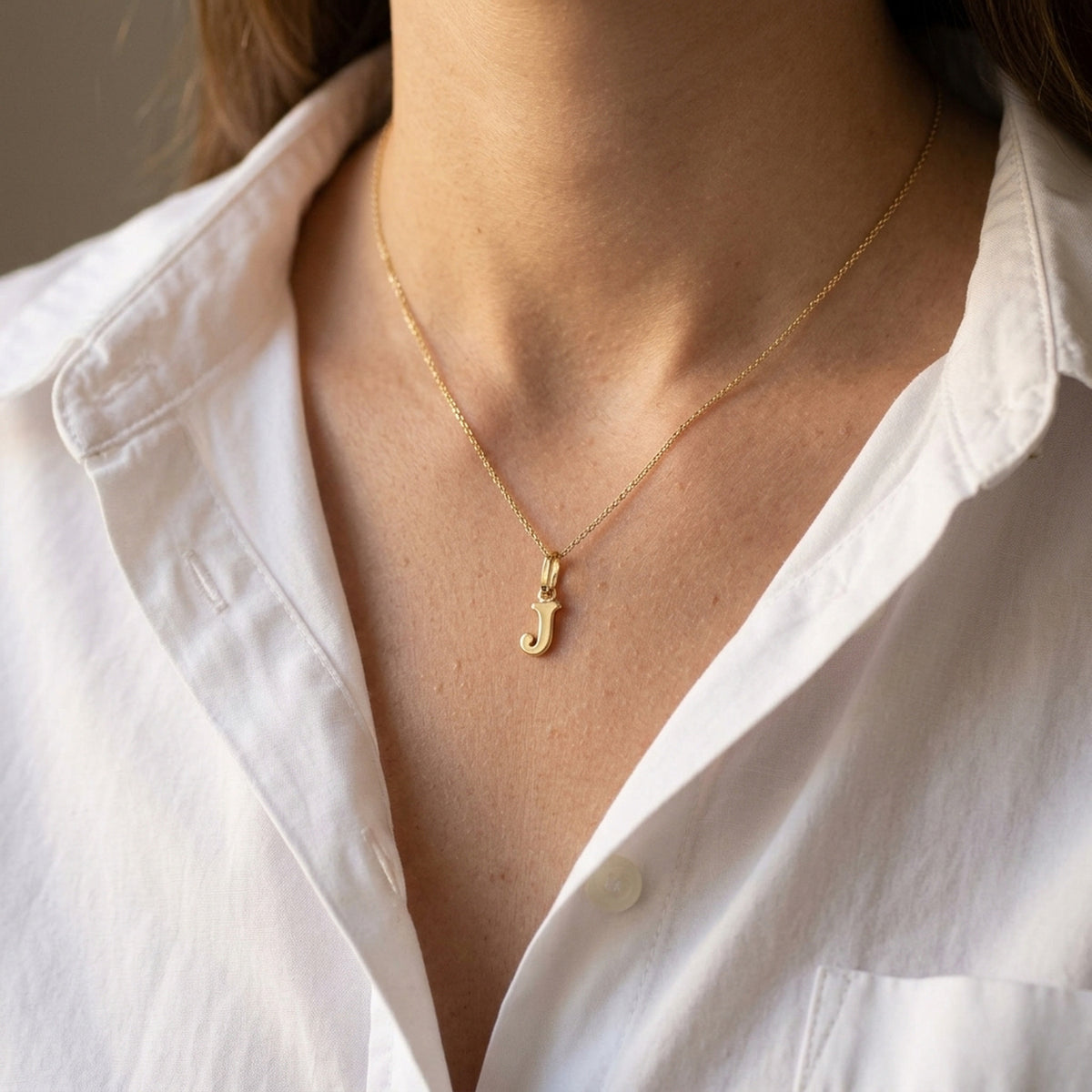 Anhänger Buchstabe J glänzend – 375er Gold, 8 × 4 mm – an einer feinen Kette getragen, natürliche Lifestyle-Aufnahme