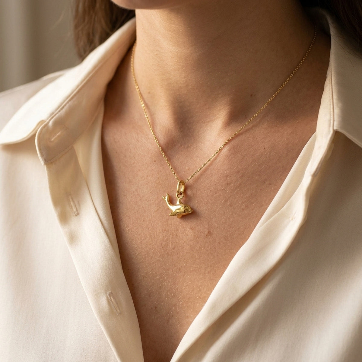 Anhänger kleiner Delfin glänzend – 375er Gold, 12 × 7 mm – an einer feinen Kette getragen, natürliche Lifestyle-Aufnahme
