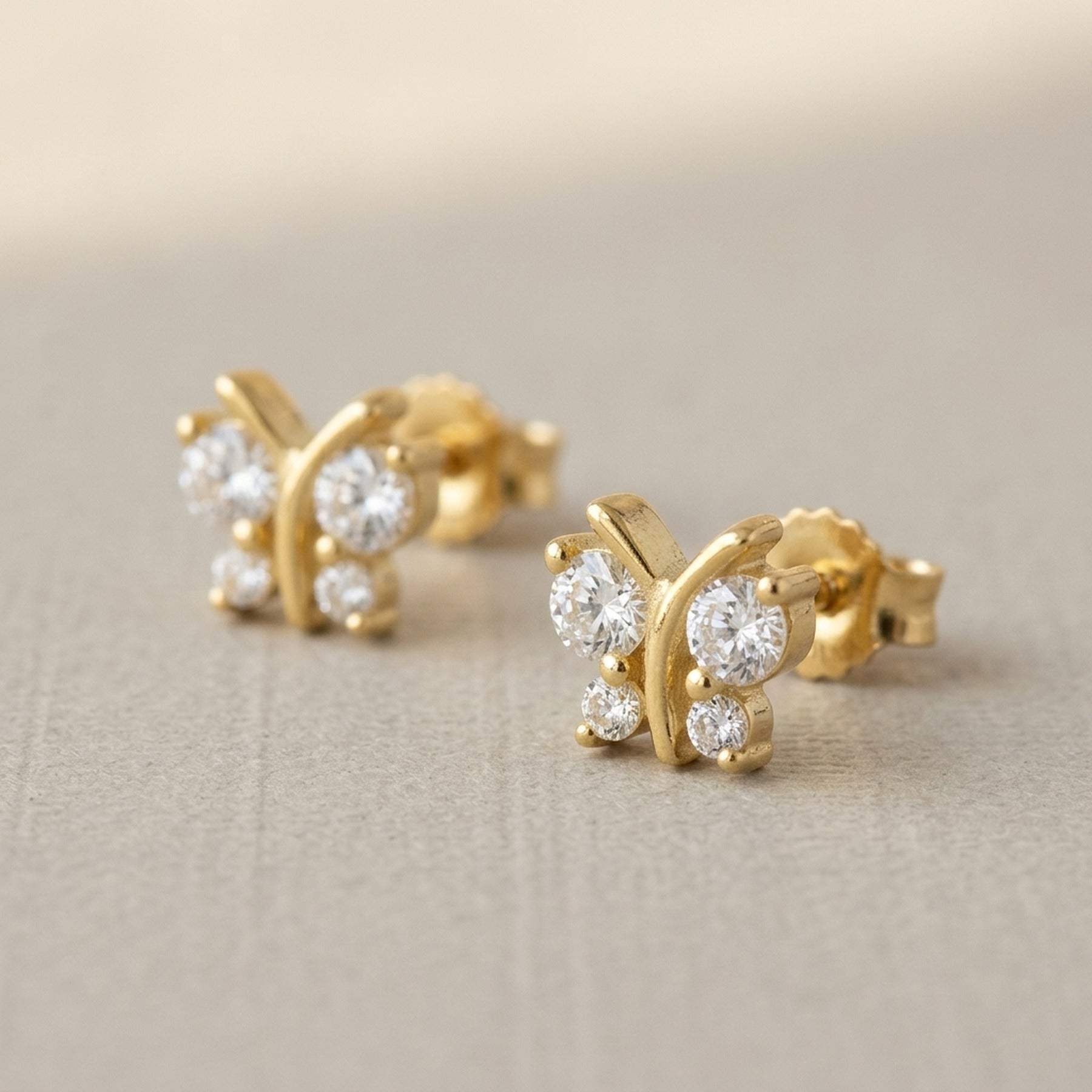 Ohrstecker Schmetterling mit 4 Zirkonia – 375er Gold, 6 × 6 mm – Detailansicht des Ohrschmucks vor neutralem Hintergrund